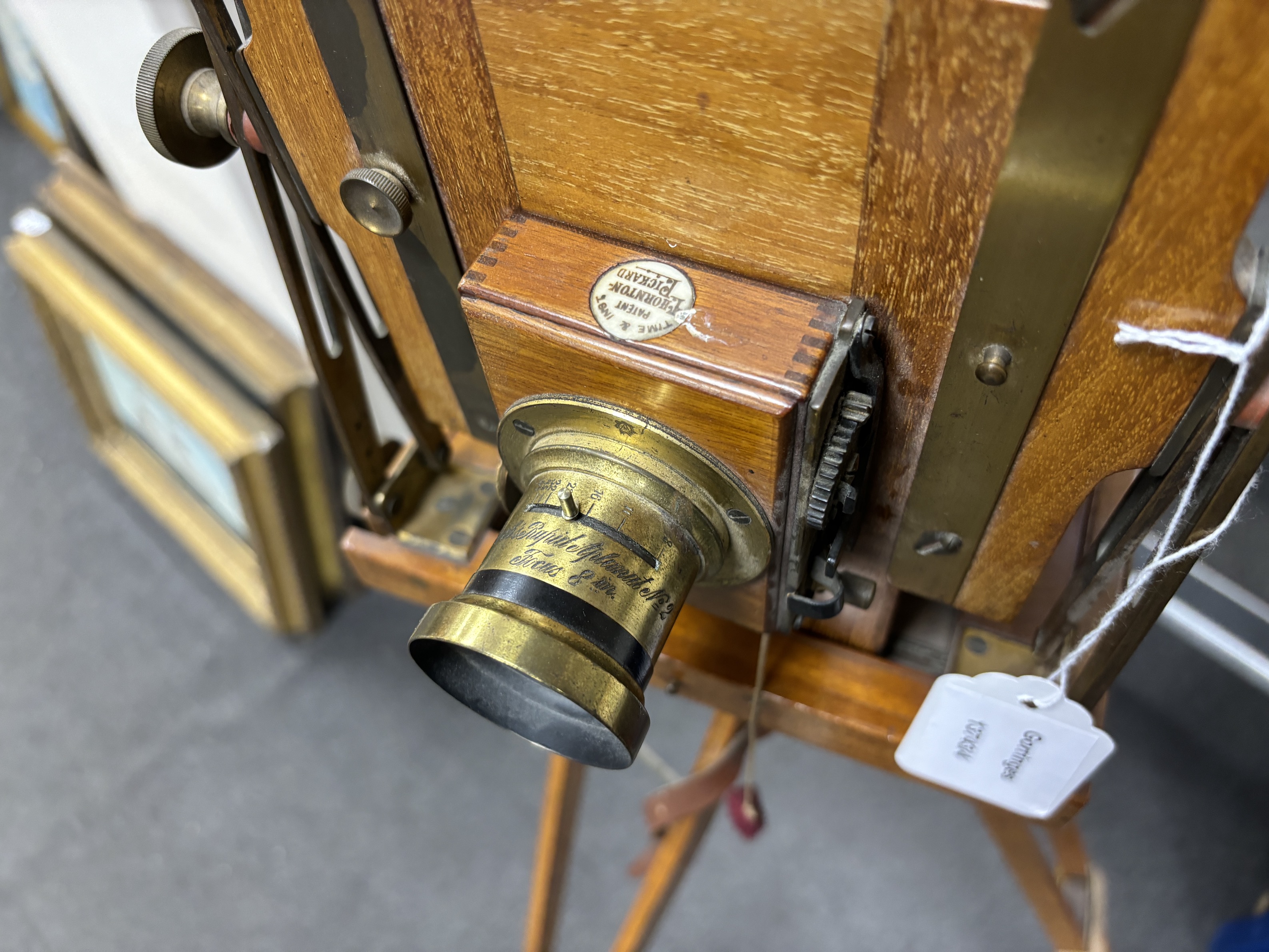An early 20th century brass and mahogany ‘Sanderson’ half plate bellows camera by G.H.&S., London, with a lens and a shutter action by Thornton Pickard, on an oak tripod
